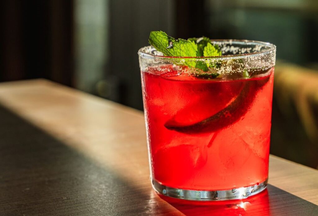 Red cocktail with mint leaf and salt rim, on a wooden table