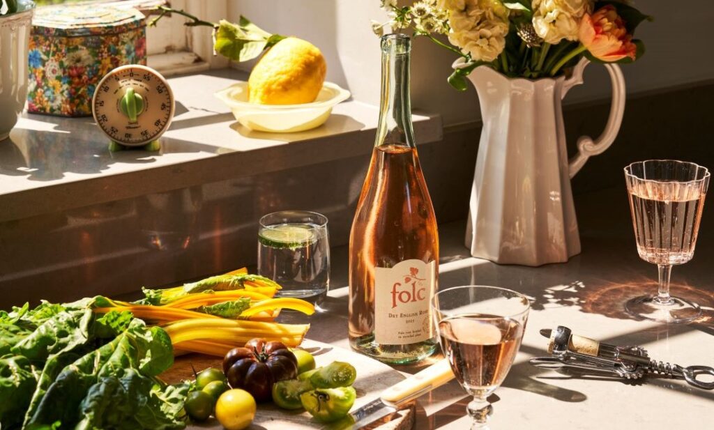 Bottle of folc rose wine next to a white jug of flowers and mixture of seasonal British vegetable